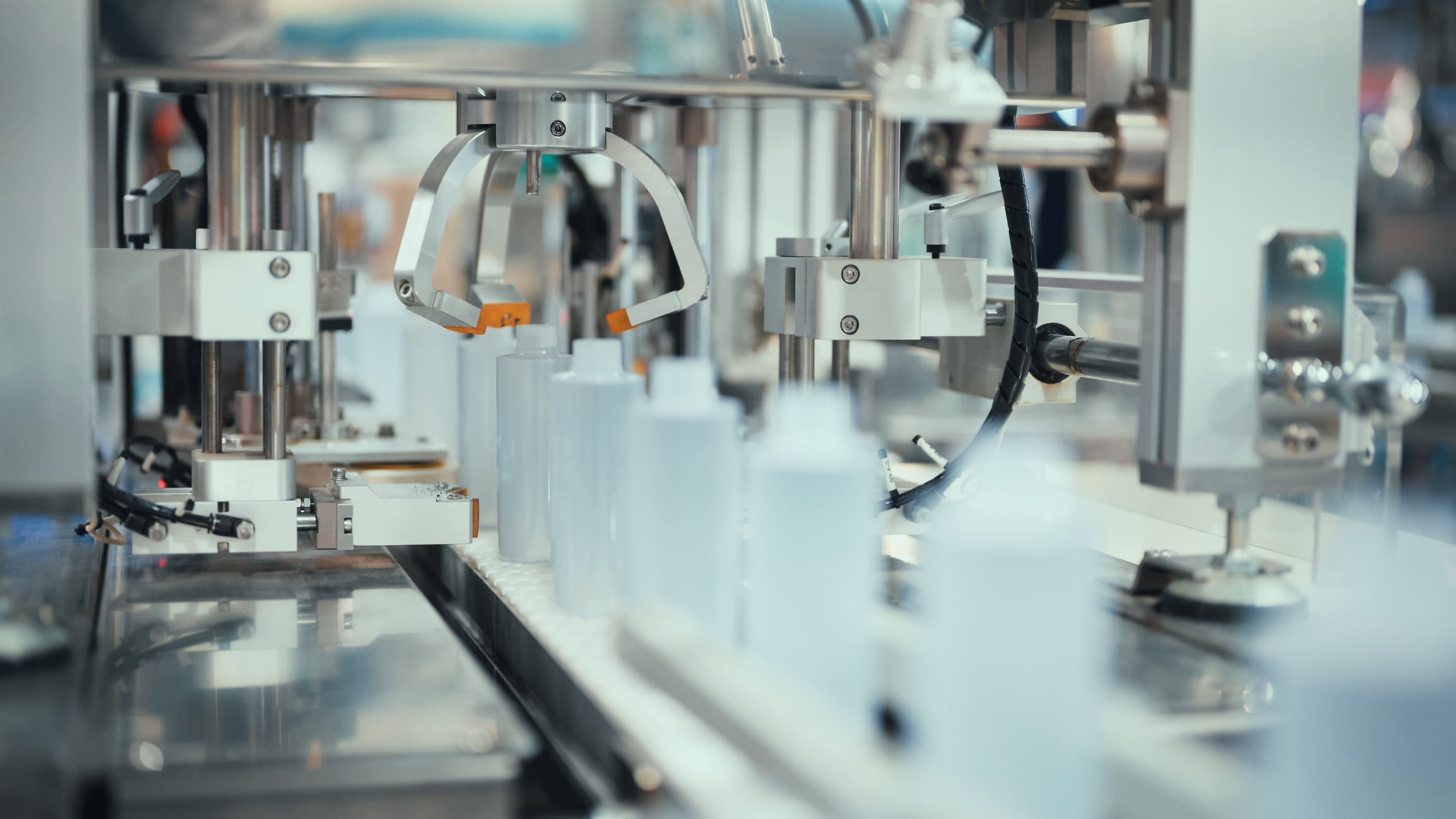 Close-up of an automated manufacturing line with robotic arms handling transparent bottles.